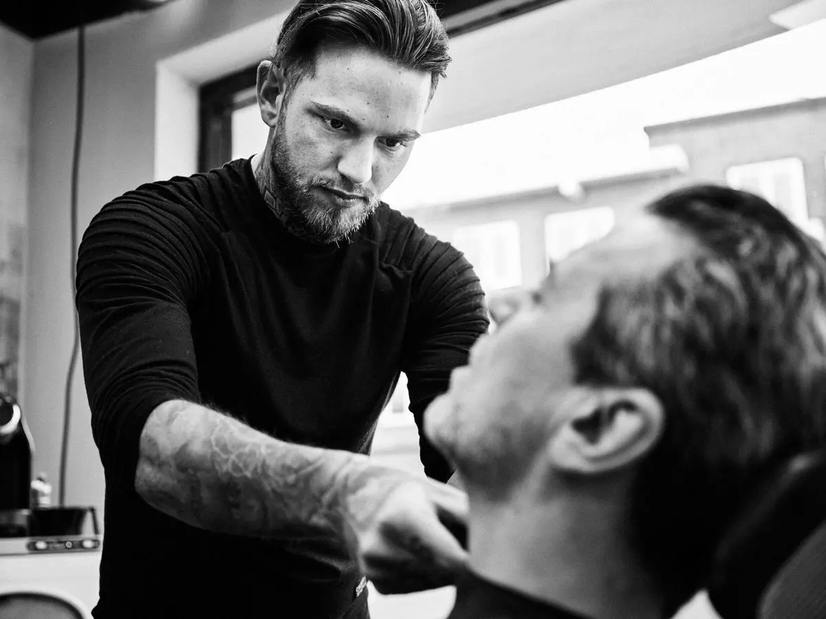Barbier werkt met een scheermes, in zwart-wit